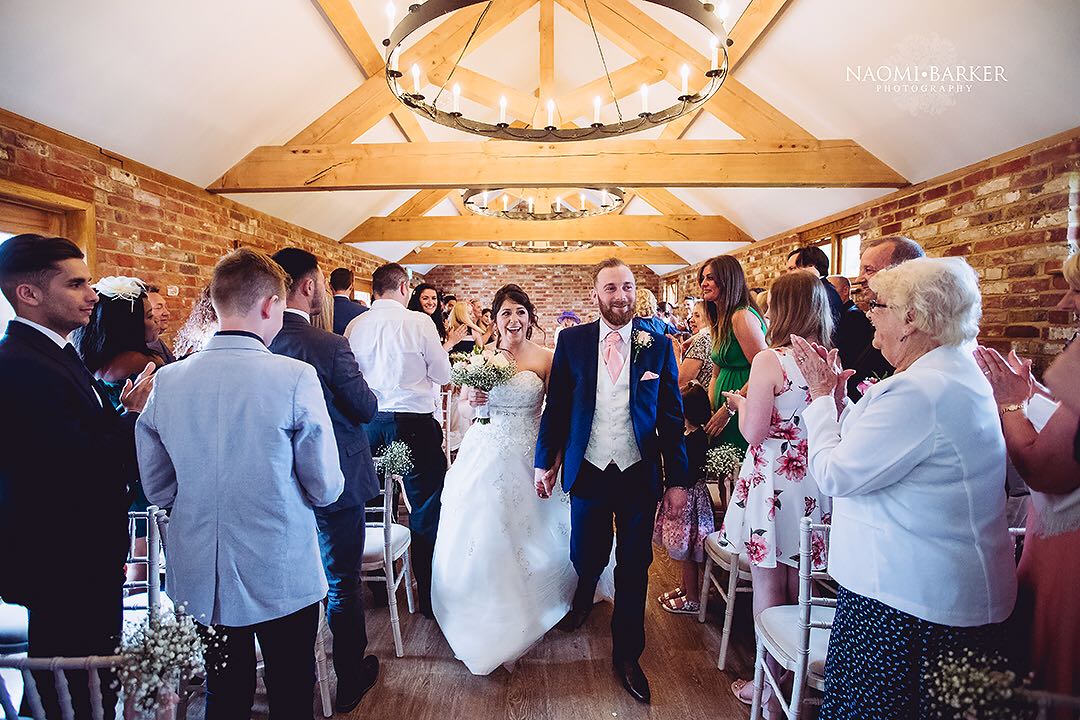 newlyweds exit their ceremony as guests cheer at apton hall wedding venue in essex