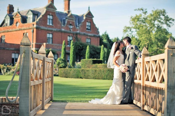 a couple kiss on a wooden bridge outside Chippenham Park wedding venue, in Cambridgeshire