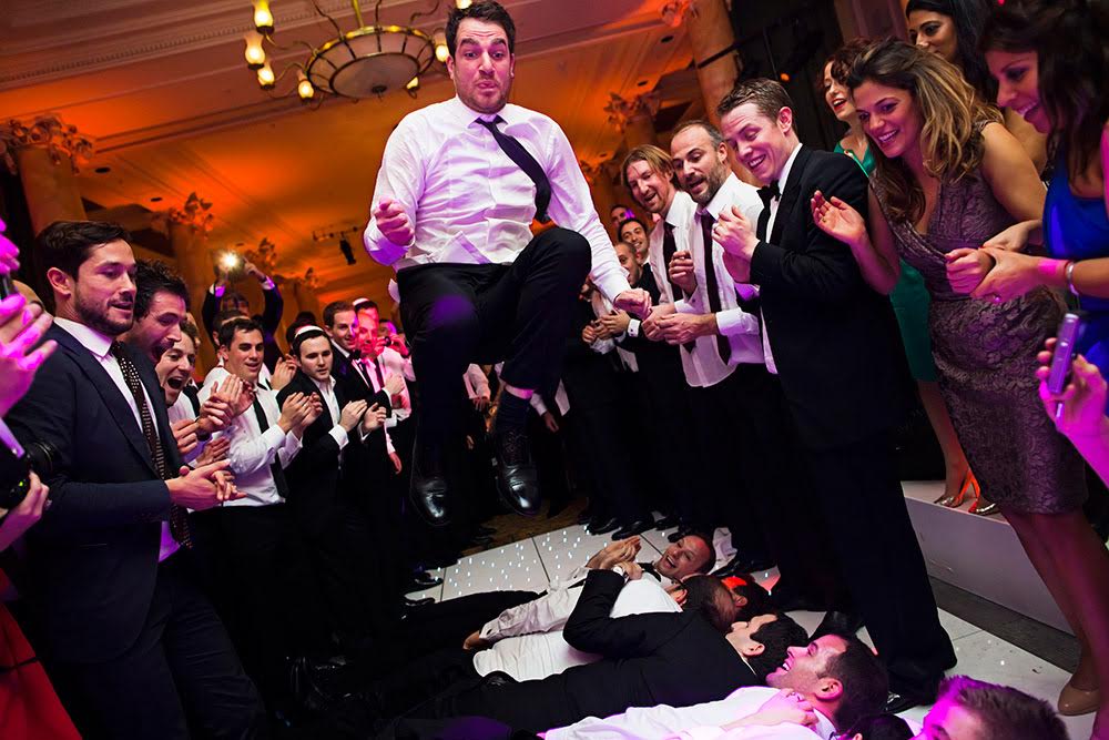 bridebook.co.uk-smashing-the-glass-groom jumping over wedding guests