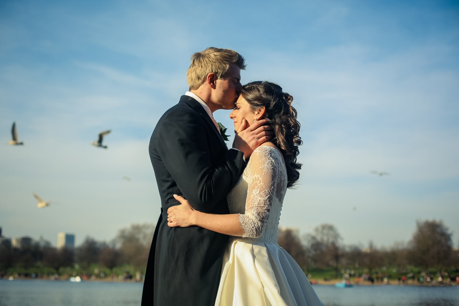 Bridebook.co.uk- groom kissing bride on the forehead by the serpentine lake