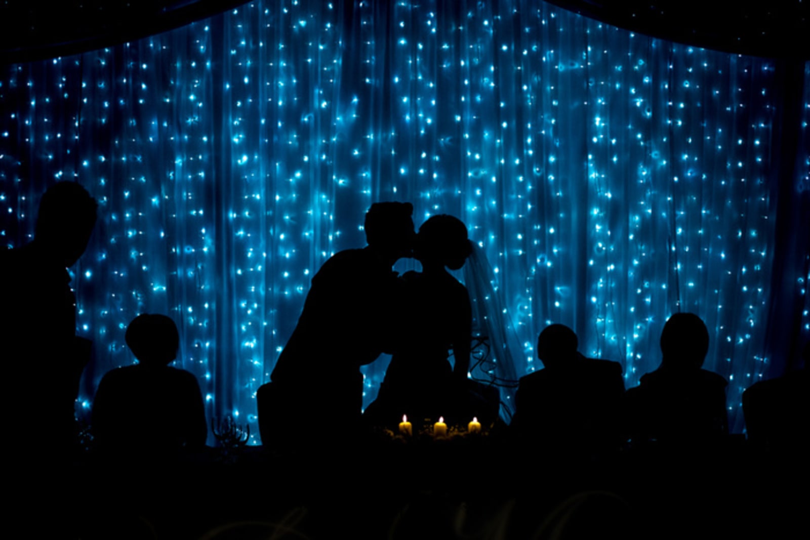 Bridebook.co.uk- bride and groom kiss against a lit up abckground