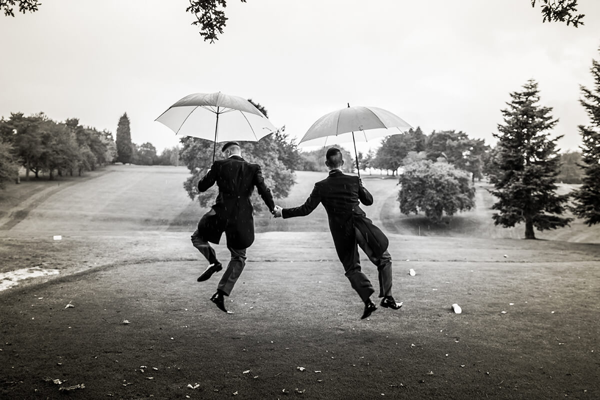 two grooms dancing with umbrellas on their wedding day