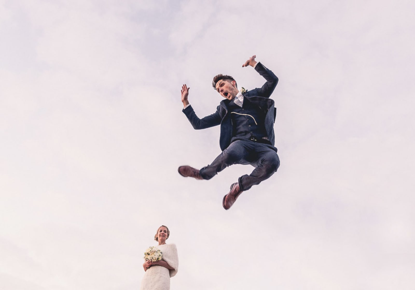Bridebook.co.uk- groom jumping in the air as bride watches